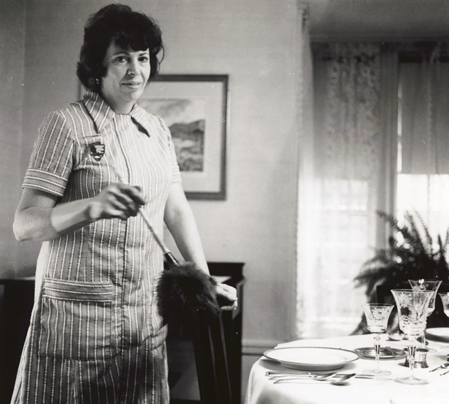 Woman in a smock with a feather duster dusts a set table