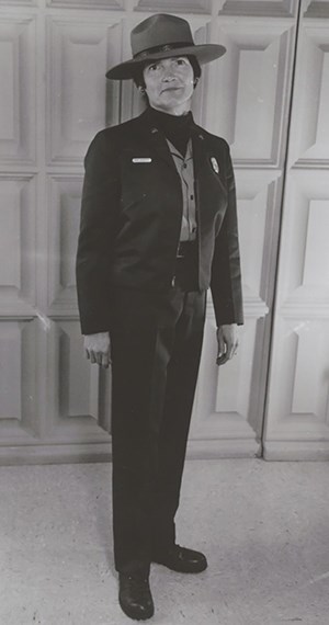 hfca_1607_hackett_marjorie_002_u_cropped Female ranger seen in traditional dress, a wide brimmed hat, short long sleeve jacket, dark dress slacks and dark oxford style shoes.