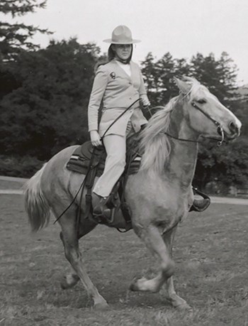 A black and white image of a woman wearing a ranger uniform and riding a horse.