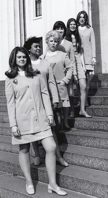 Six women stand in a line going up the stairs facing us.