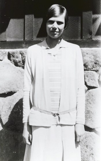 hfca_1817_ashton_ruth_u_003 Ruth Ashton wears a long skirt, a collared blouse and belted cardigan stands facing the camera.