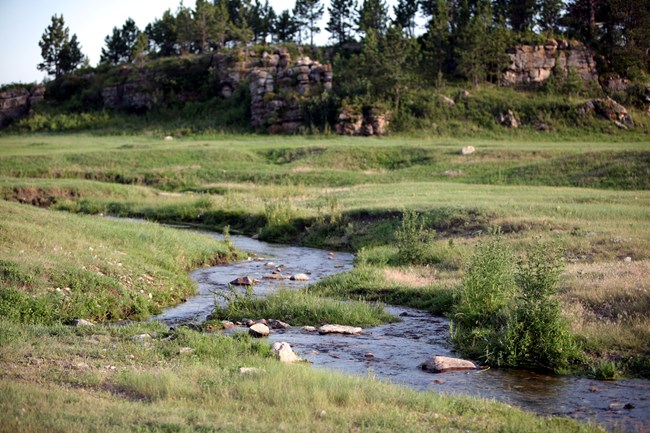 a shallow stream meanders through prairie with a rocky outcrop in the background