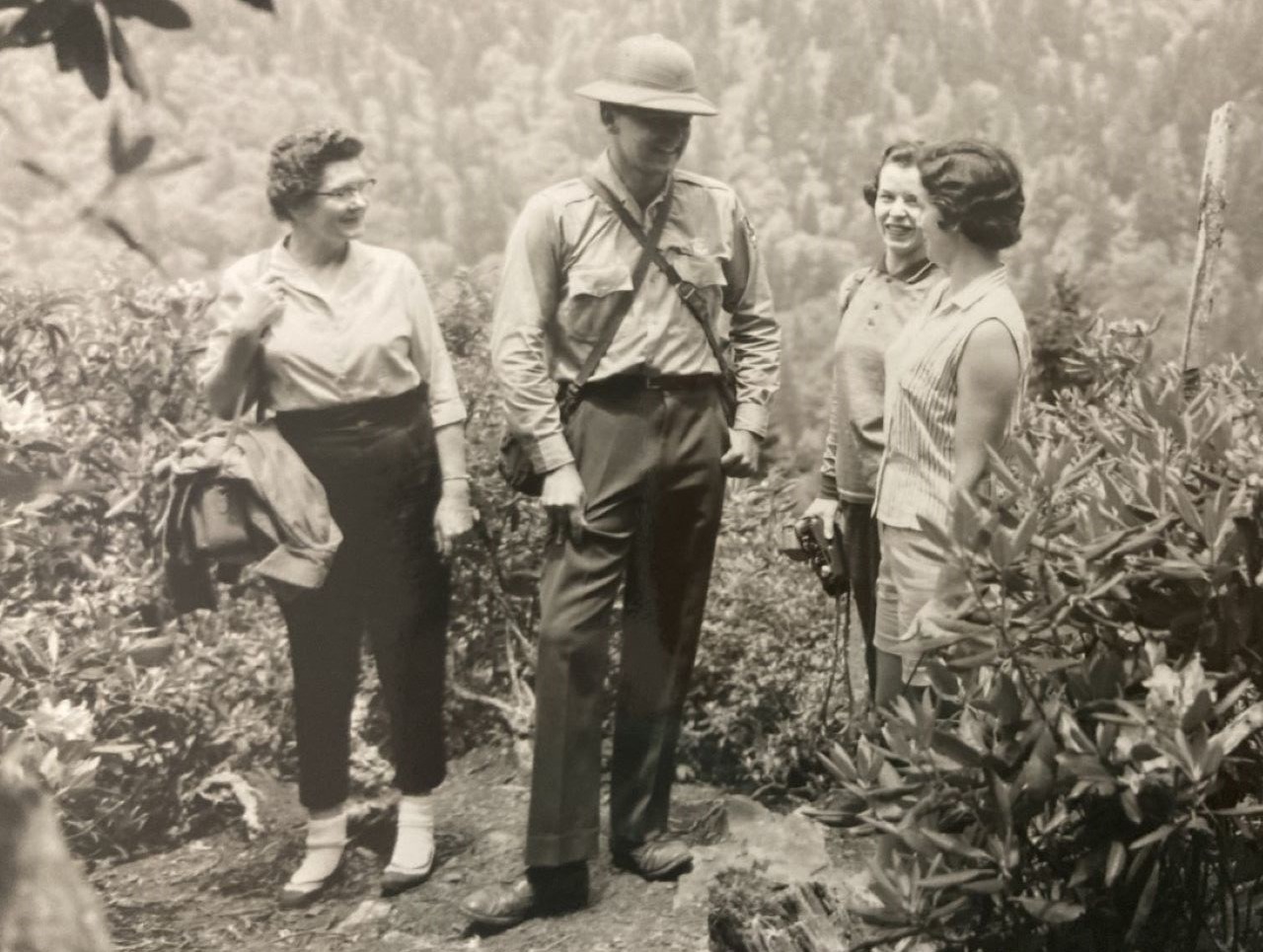 Ranger wearing a sun helmet stands talking with three women on a hiking trail.