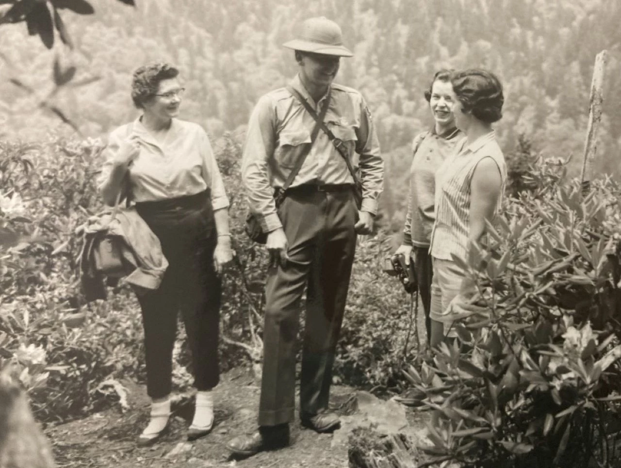 Ranger in a sun helmet on a hike Ranger wearing a sun helmet stands talking with three women on a hiking trail.