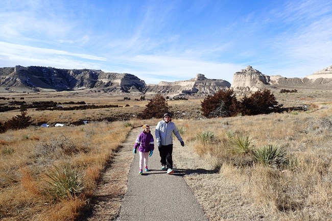 A pair of hikers ascends a rocky bluff on an asphalt trail.