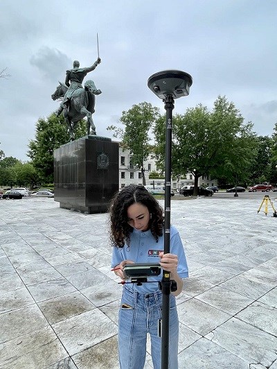 woman using a gps instrument for measured drawings of statue in the background