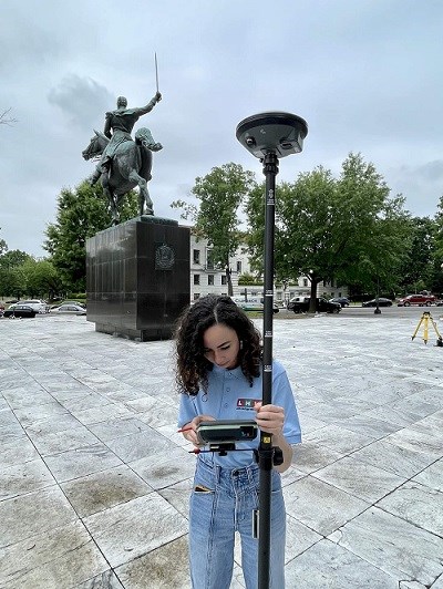 Hillary Morales Working at Park woman using a gps instrument for measured drawings of statue in the background