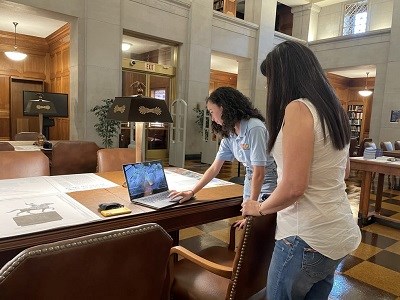 two women look at drawings of the simon bolivar statue and at a video of the statue on the computer
