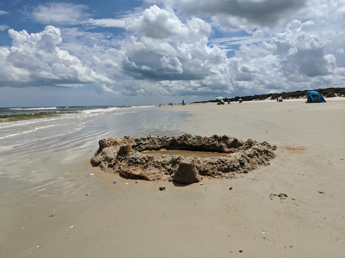 Sand castle hole on Fort Matanzas beach with ocean and duens in background.