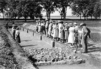 A row of visitors looks down at two rangers standing in a excavations site.