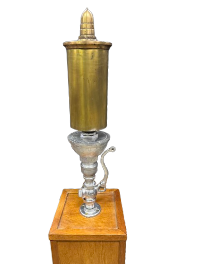 SMI Steam Whistle A gold, cylindrical tube with a silver base sits on top of a wooden pedestal.