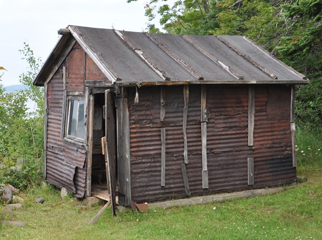 Historic rusty corrugated iron shack with a glass window and rickety open door.