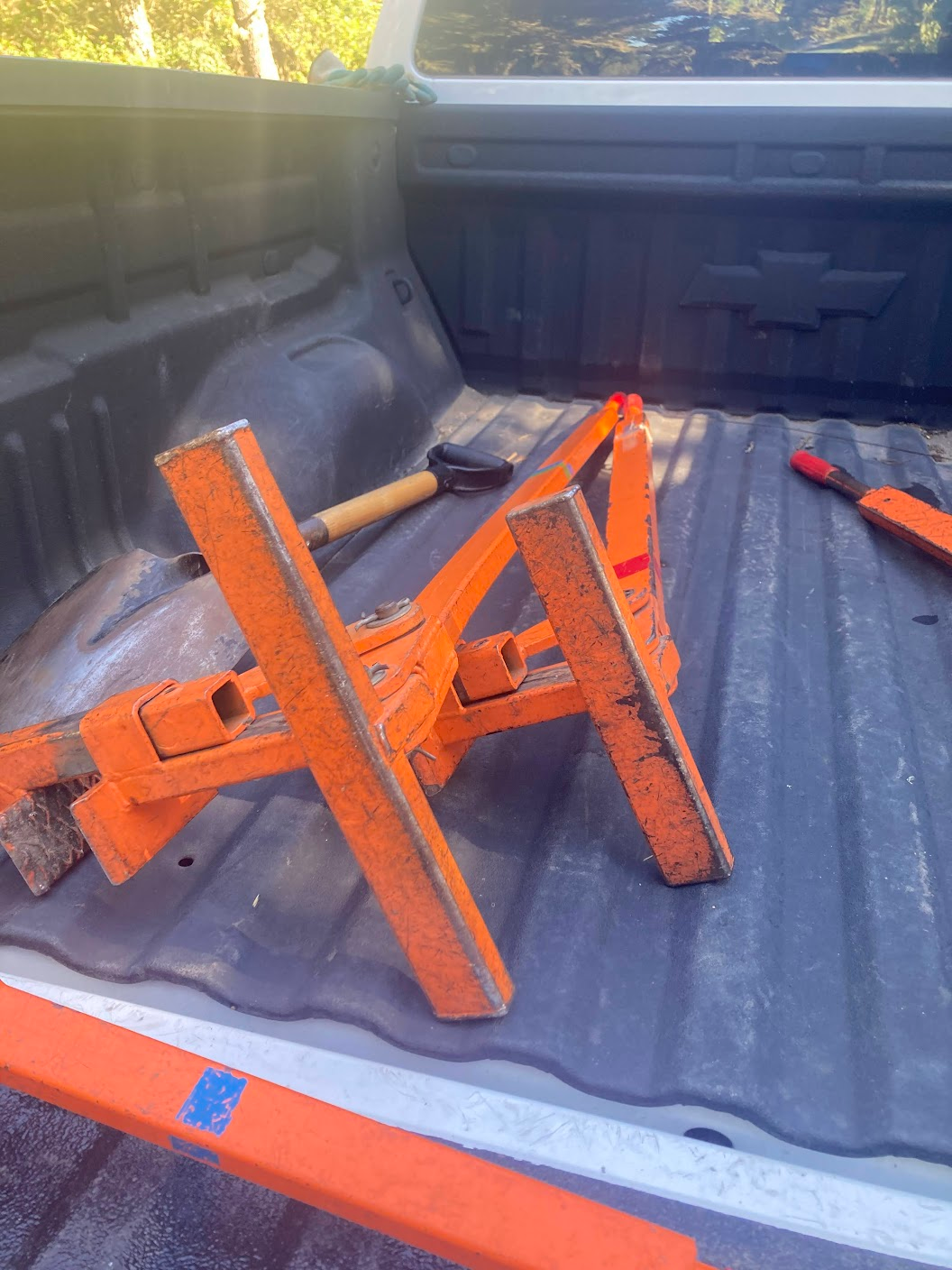 A large, metal lever-like contraption in the back of a pickup truck. It's mostly bright orange, but the paint is scratched and worn in several places.