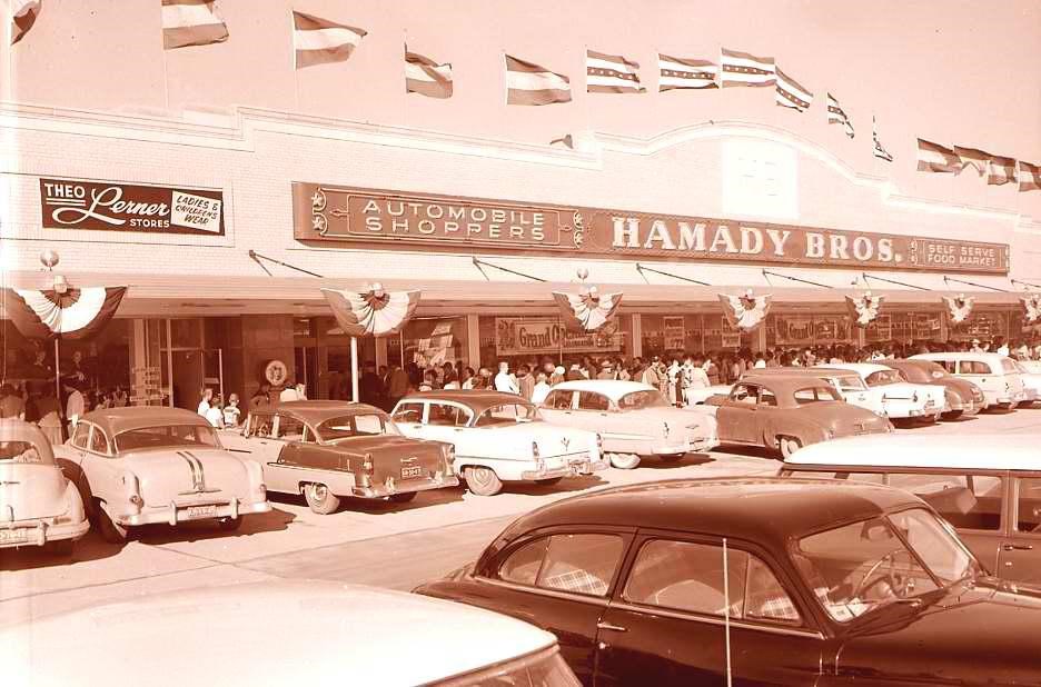 A sepia-toned photo of a parking lot full of cars in front of a grocery store