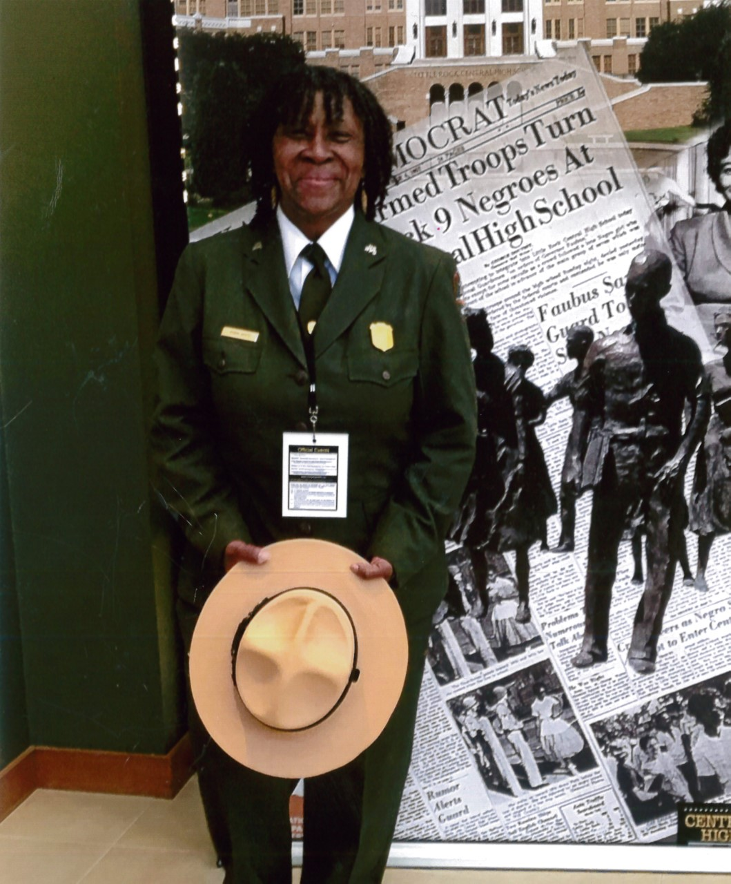 Superintendent Robin White Robin White poses in her NPS uniform in front of an exhibit panel about Little Rock High School. She holds her ranger hat in her hands.
