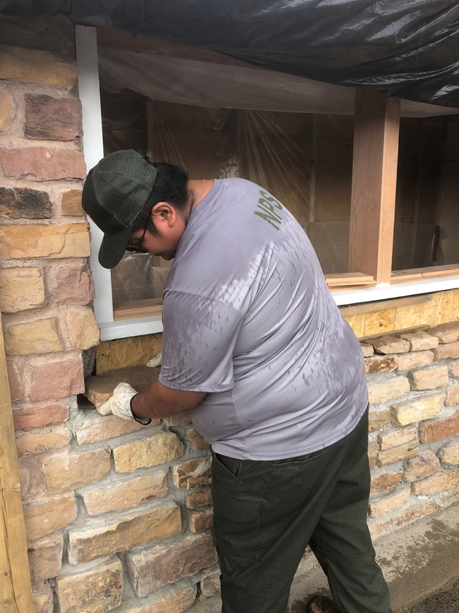A man in an NPS uniform replaces bricks in the wall of a historic building.