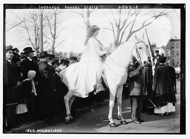 a woman dressed in white on a white horse surrounded by people in dark clothing 1913 Library of Congress