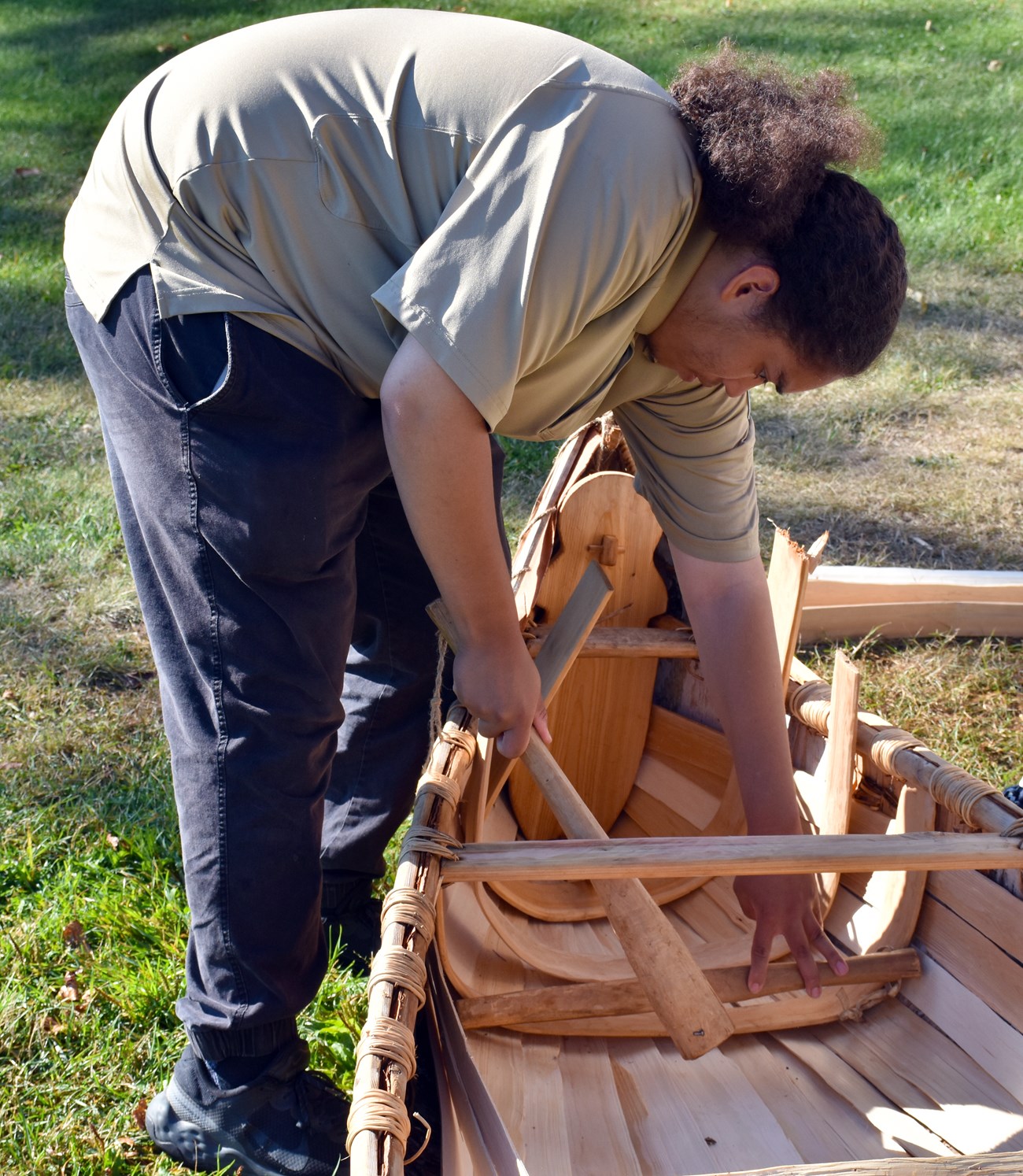 installing ribs A person uses a wooden tool to hammer a cedar rib into place on the interior of a canoe.