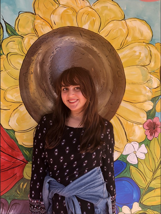 A woman stands in front of a wall with a painted sunflower