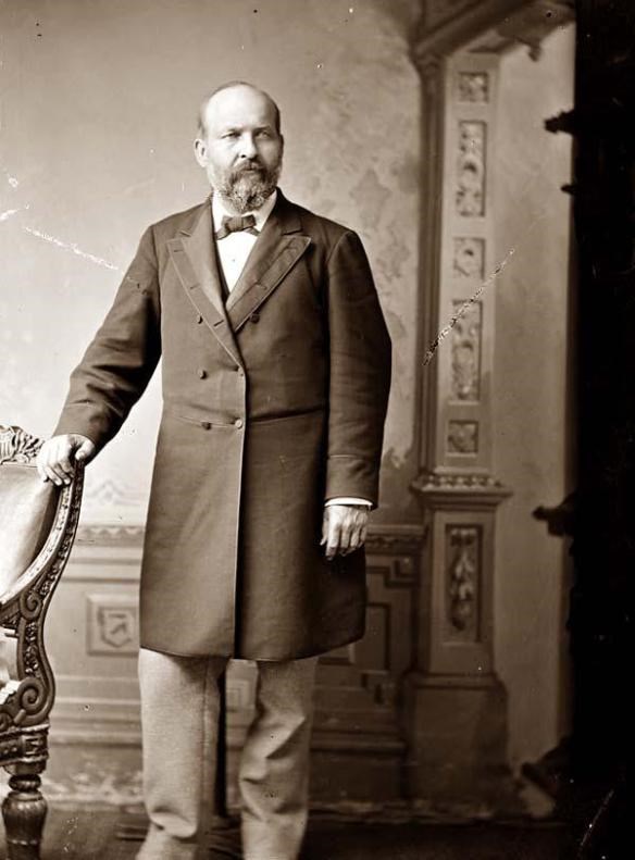 jag-pres-standing James standing with his left hand on the back of a chair