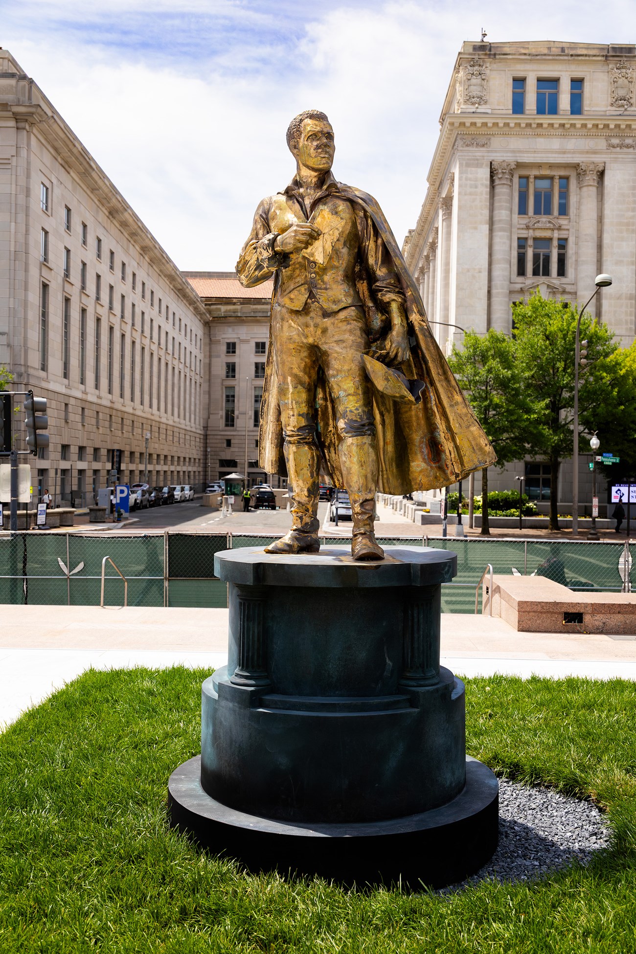 Gold toned statue of a man in a long cloak holding a tri-corner hat and an envelope