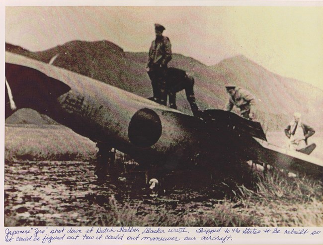 Japanese Zero Plane, shot down Upside down plane with circle on side, with soldiers standing on top of it.
