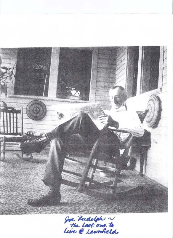 joe-r man with glasses sitting in a rocking chair on a porch while reading the paper