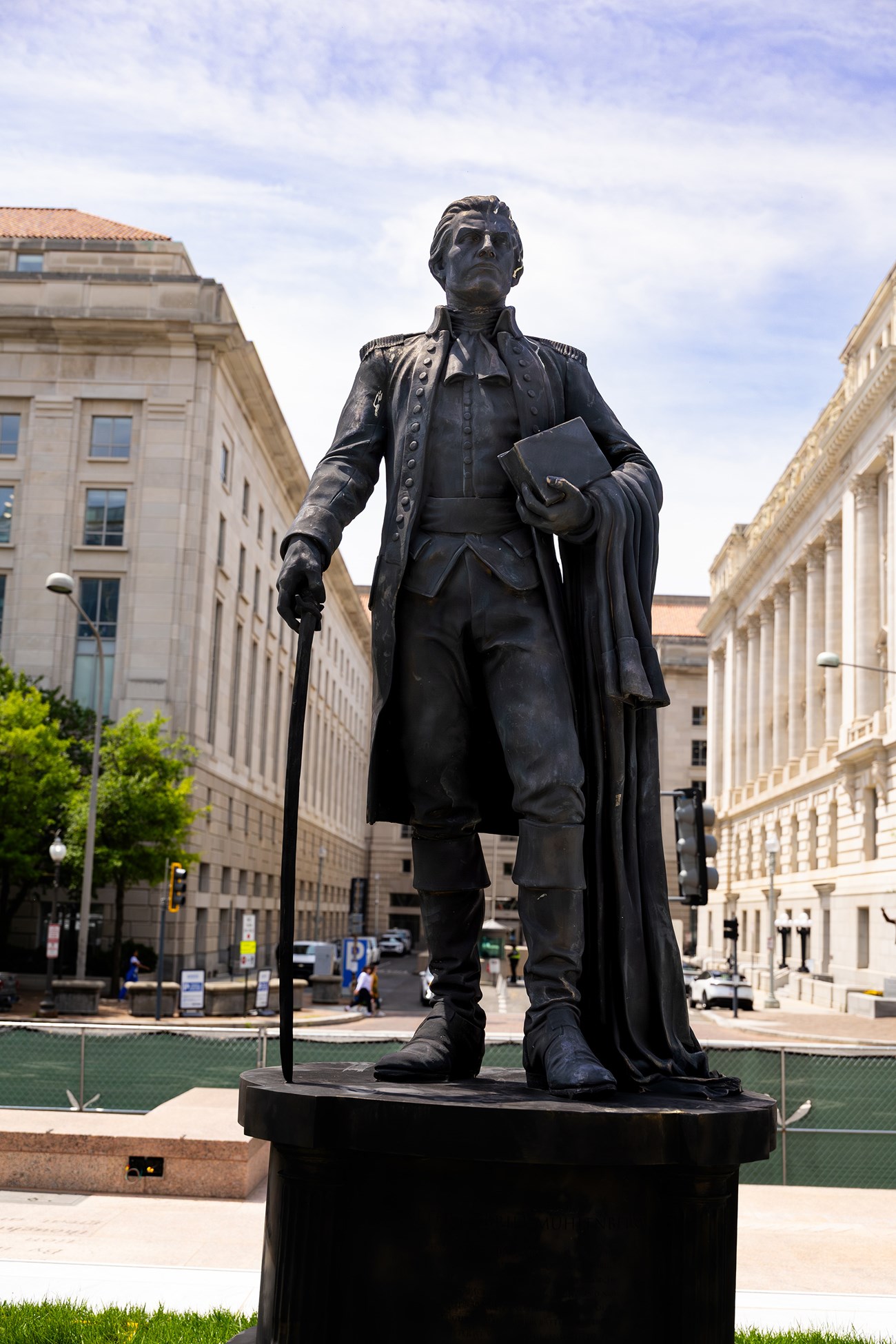 Dark bronze statue of a man holding a book, cloak and saber