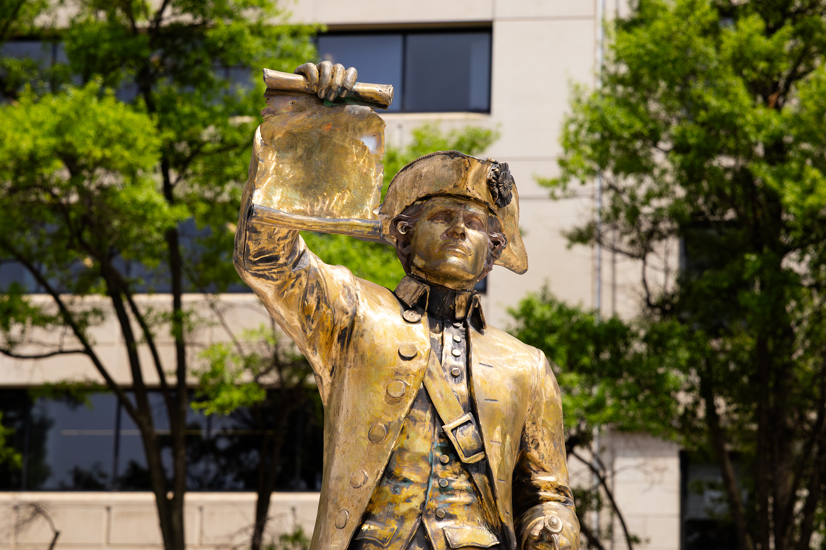 Gold toned statue of a man in a tri-corner hat holding up a scroll