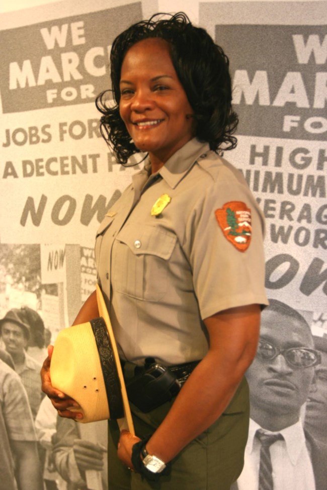 Judy Forte in uniform holding her flat hat standing in front of images of demonstration signs.