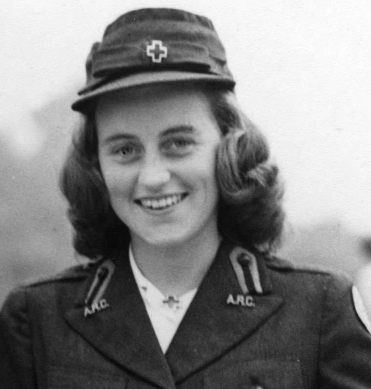 A black and white photo of a smiling young woman from the shoulders up, in a blazer with pins spelling “ARC” on each lapel, a cap with a metal pin in the shape of a medical cross, and the same pin on her collar. Her hair is curled in waves.
