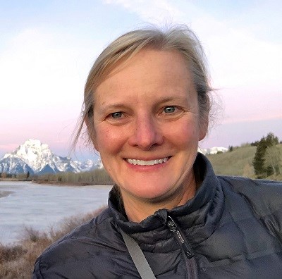 Kirsten King a woman smiles at the camera with snowy peaks in the distance behind her