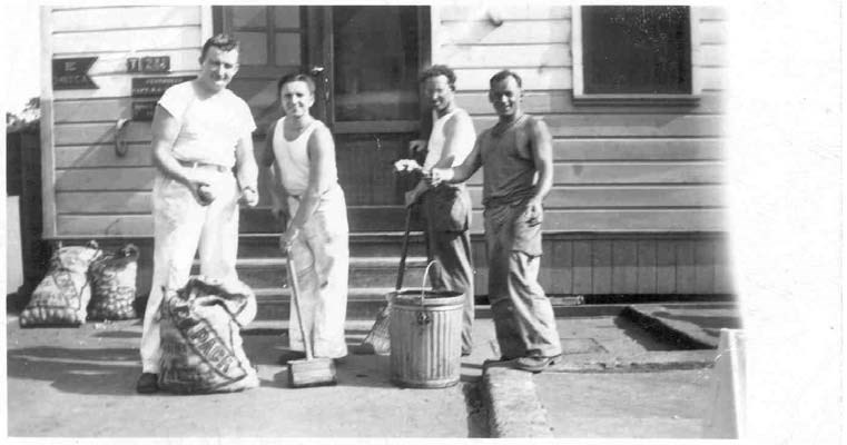 four men standing around a large pail and sack of potatoes