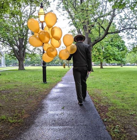 A park ranger walks down a path holding balloons