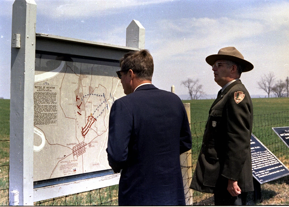 President Kennedy at Antietam National Battlefield Kennedy and a uniformed Park Ranger observe a park map.