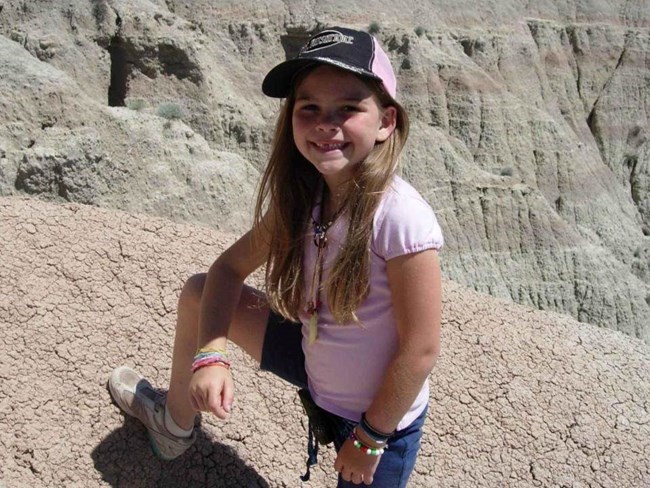 a young girl in a pink shirt smiles as she climbs a badlands butte.