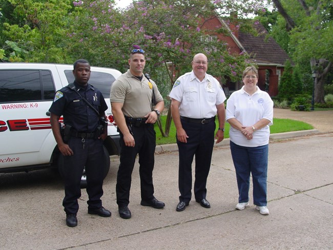 Three people in uniform and a fourth in a white polo and jeans stand next to eachother posing for a picture.