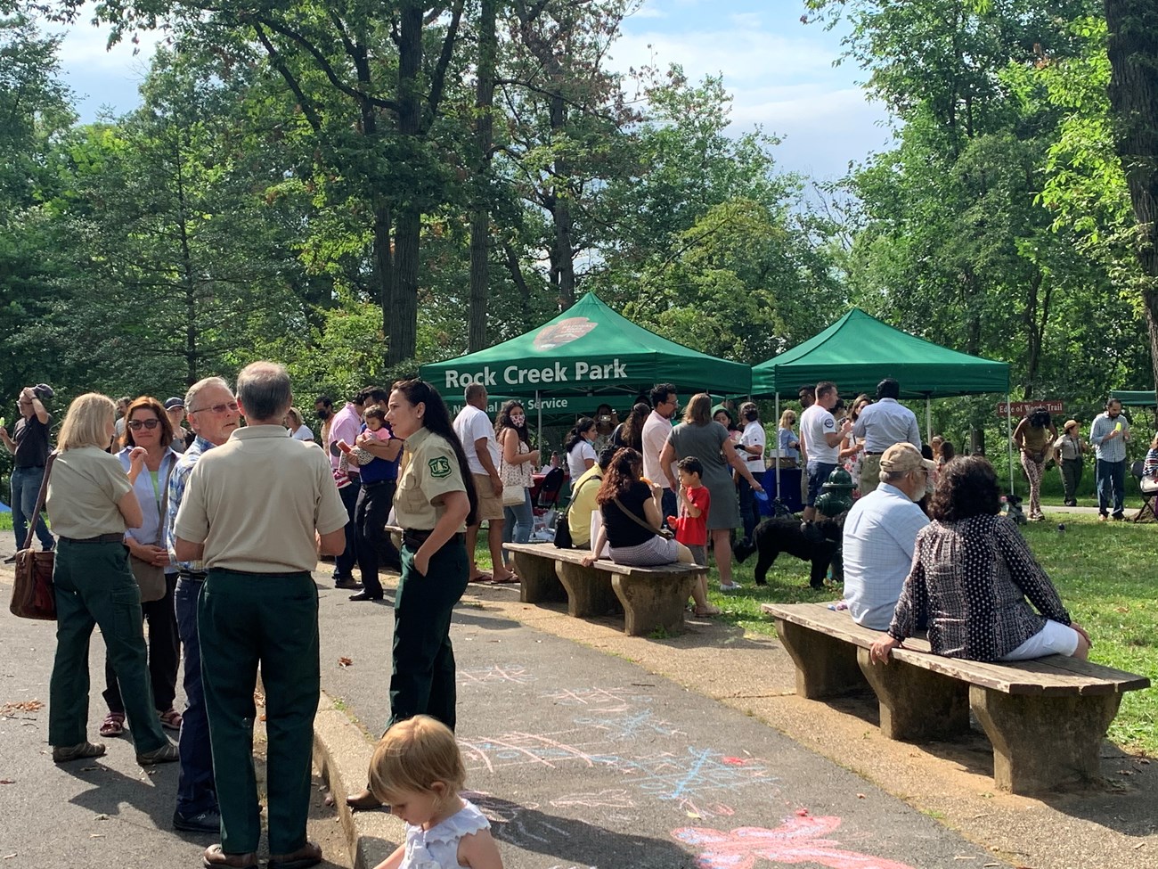 People mingle in a grassy area near pop up tents with the NPS logo