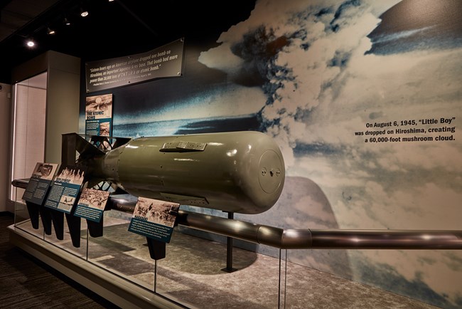 Display at the former K-25 uranium-enrichment plant, now a history museum, in Oak Ridge, TN. Museum display with a missile against a photo of a mushroom cloud with labels with text in the foreground.