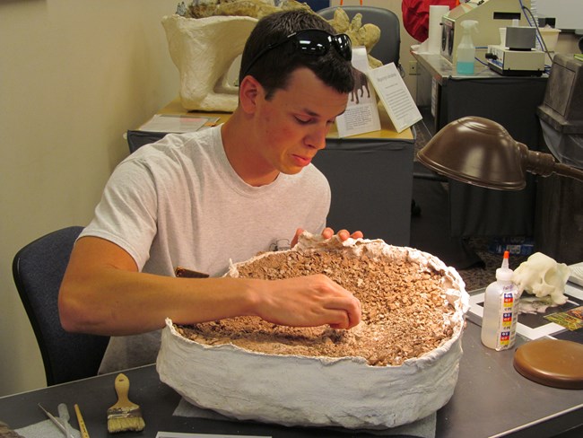 a young man holds a large brown rock surrounded by white plaster.