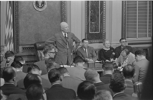 Black and white image of President Eisenhower surrounded by reporters.