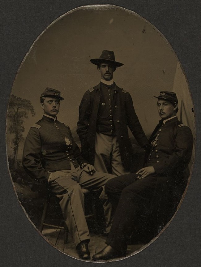 Photograph shows a full-length portrait of three officers of the 54th Massachusetts Infantry Regiment. Sitters have been identified as Second Lieutenant Ezekiel Gaulbert Tomlinson, Captain Luis F. Emilio (center), and Second Lieutenant Daniel G. Spear (Na