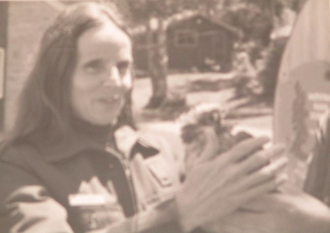 Lynda Boose with falcon chick Lynda Boose in her NPS uniform touches a peregrine falcon chick held in someone else's hands.