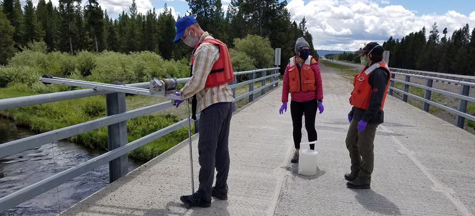 Three scientists on a bridge using a pulley to sample water in the river below.