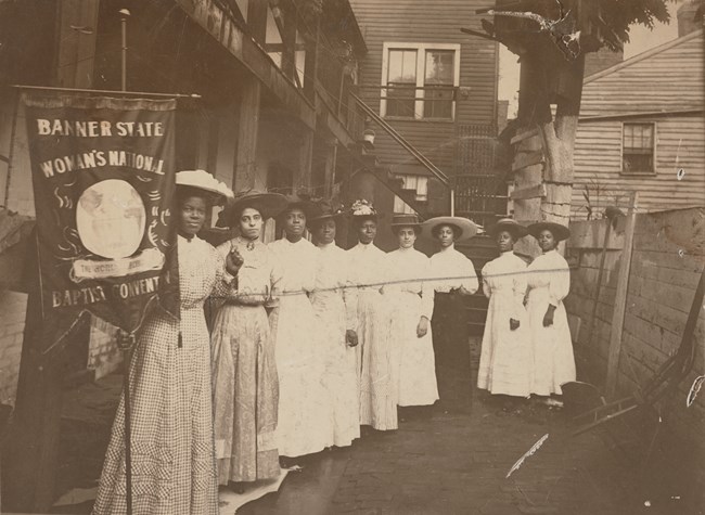 Nannie Burroughs and other African American suffragists, early 1900s Nine African American women standing in a row holding a suffrage banner