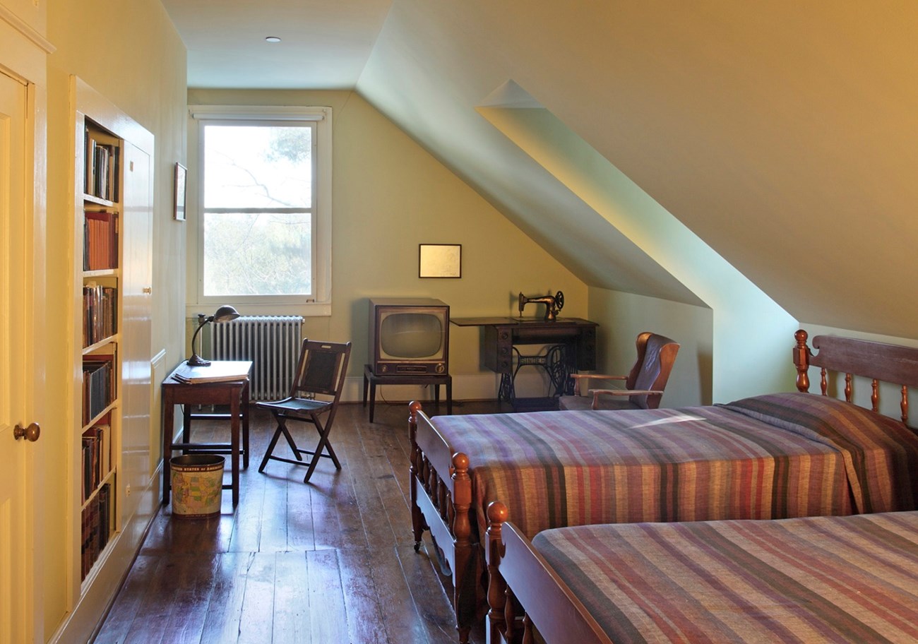 A loft bedroom with two twin beds, a tv, sewing machine, desk and bookshelves.