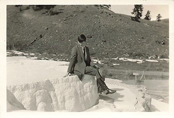 Marguerite Lindsley poses on a geological formation wearing her NPS uniform and holding a broad-brimmed hat in her hand.