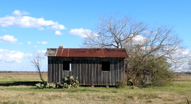 A small abandoned wooden building in an open field landscape in Guadalupe County, Texas.