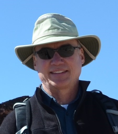 a man in hat and sunglasses smiles outdoors