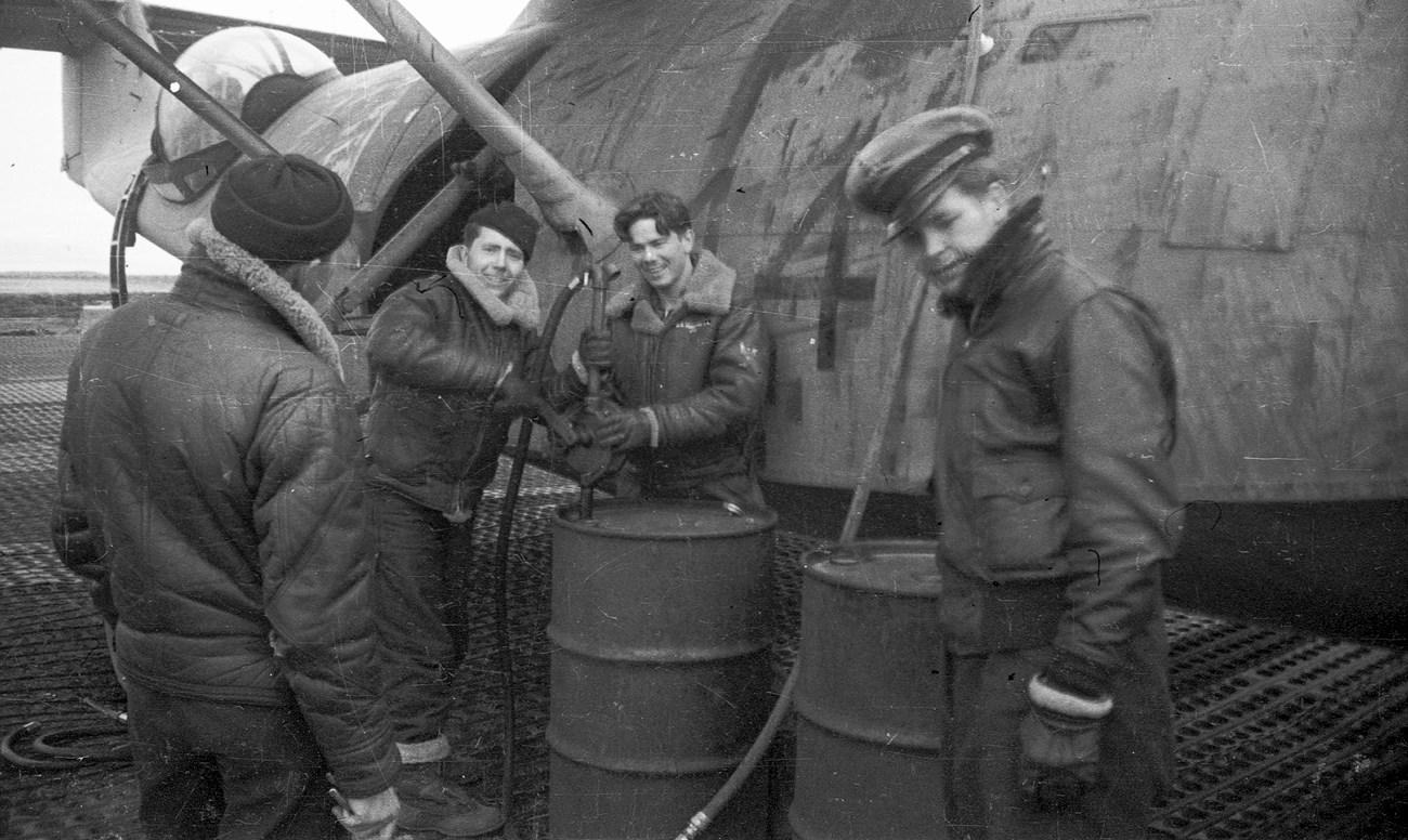 Men Refueling a Plane Four men standing around barrels of fuel, hoses, and a plane.